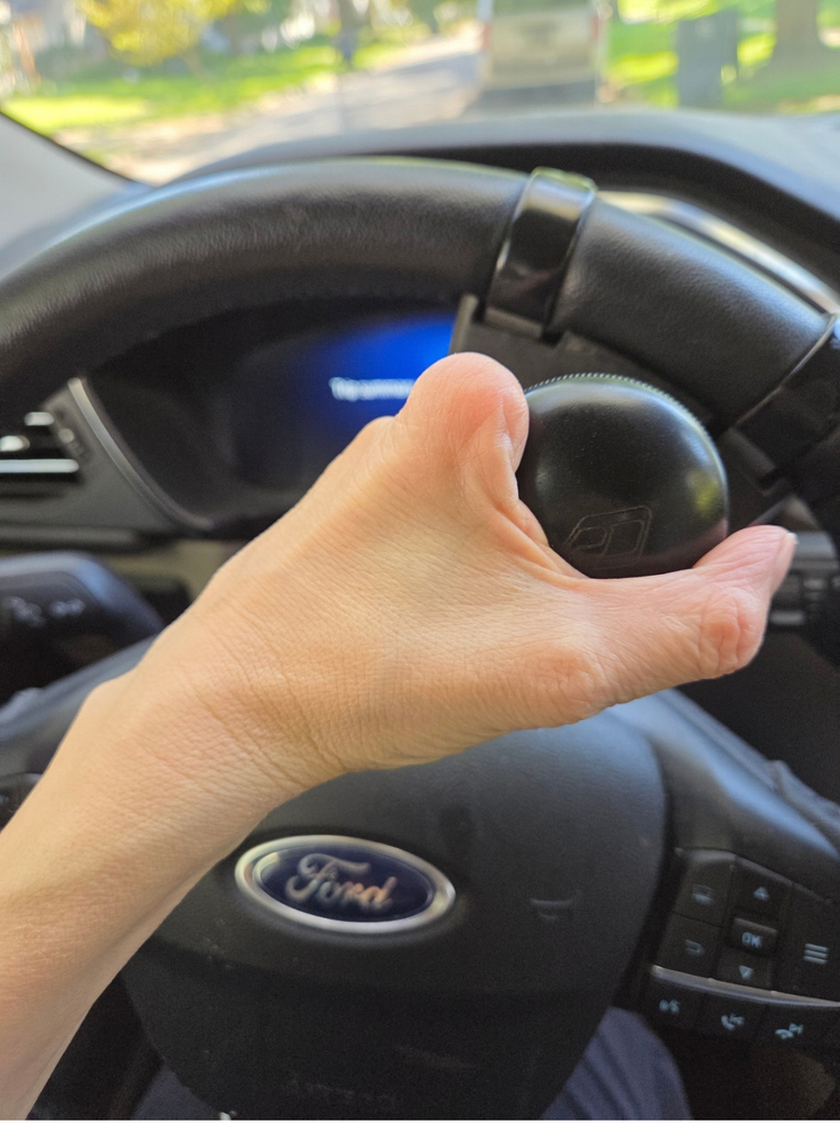 Photo of Laura's partial hand on a driving knob attached to her steering wheel